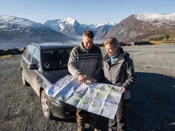 Two drivers consulting a paper road map beside their car at a high-altitude Norwegian rest area in natural daylight