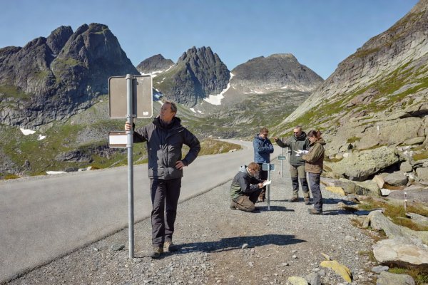 Driver standing beside a Norwegian mountain pass elevation sign in clear natural daylight